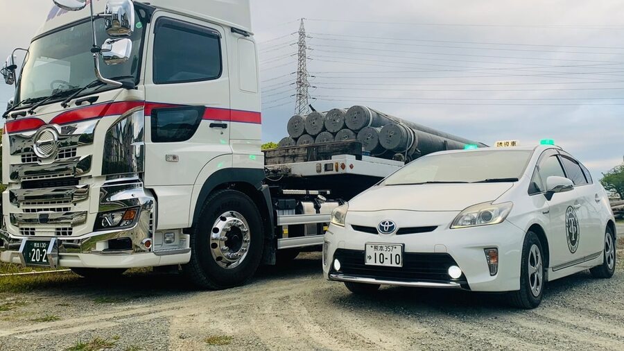 電柱を積載した輸送車と、その前方を走る先導車